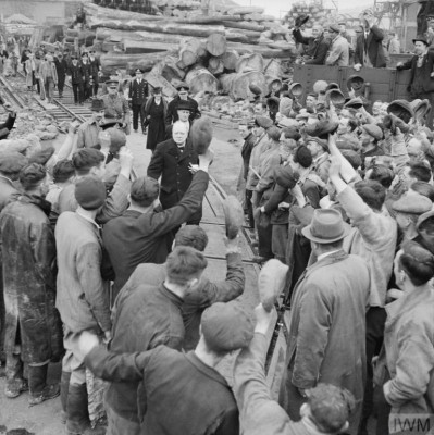 Winston Churchill, accompanied by Viscountess Astor, is cheered by workers during a visit to bomb-damaged Plymouth, 2 May 1941. Copyright: © IWM.
