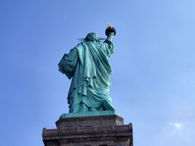 Liberty is depicted with a raised right foot, showing that she is walking forward amidst a broken shackle and chain.